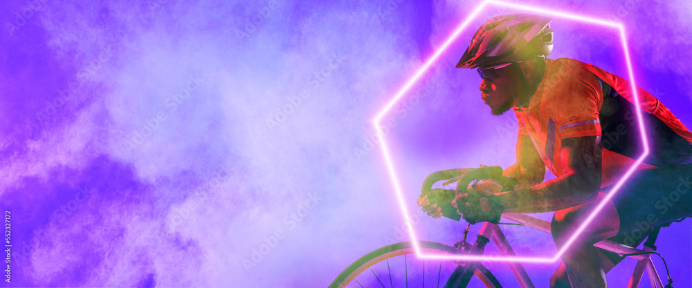 African american male cyclist riding bicycle with illuminated hexagon on purple background