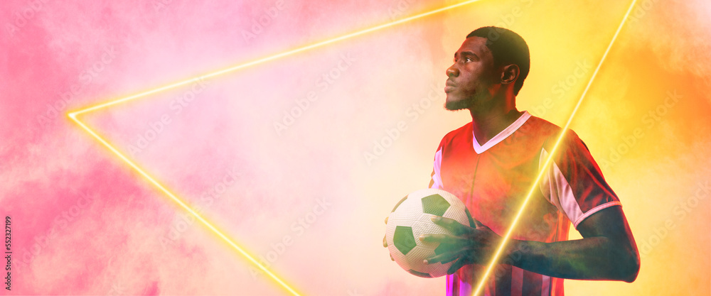 African american male soccer player holding ball and standing by illuminated triangle, copy space