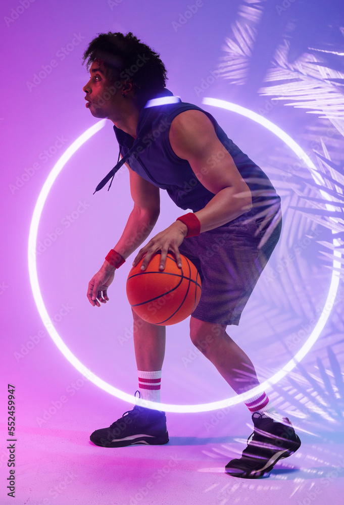 Side view of biracial male player dribbling basketball by illuminated circle and plants, copy space