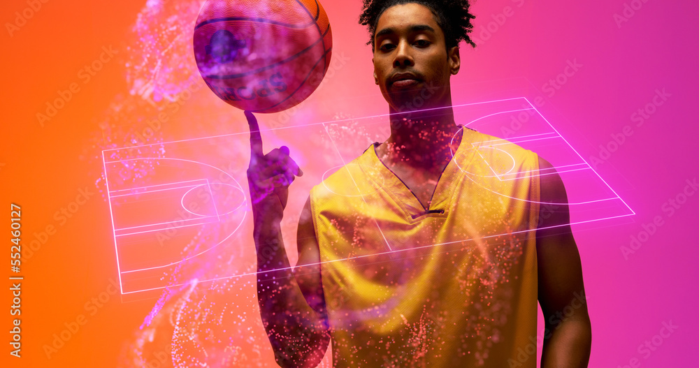 Portrait of biracial confident male player spinning ball on finger over illuminated basketball court