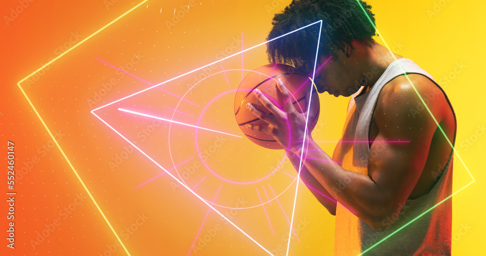 Side view of biracial player with basketball standing over illuminated multiple geometric shapes