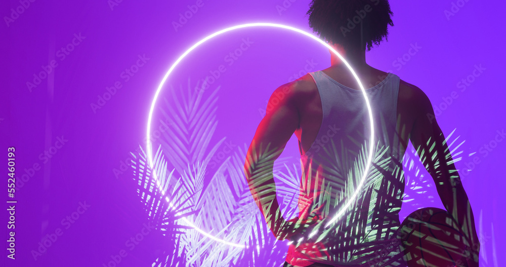 Rear view of biracial basketball player with ball standing by circle and plants on purple background