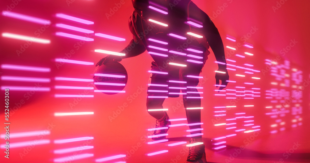 African american basketball player dribbling ball by glowing lights on red background, copy space