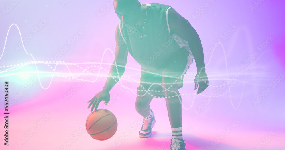 African american basketball player dribbling ball by illuminated wave patterned lines