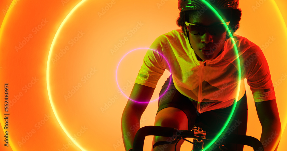 Biracial female athlete wearing glasses and helmet riding bike over illuminated colorful circles