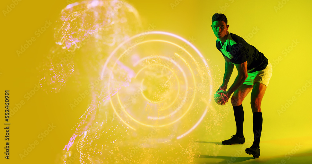 Caucasian rugby player throwing ball by illuminated circle and abstract pattern on yellow background