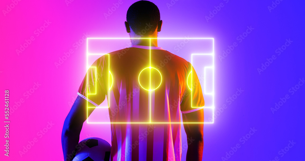 Rear view of african american male player with ball and illuminated soccer field on color background