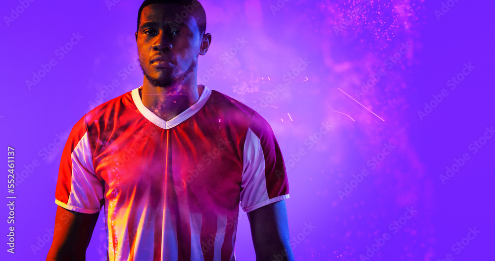 Portrait of serious african american male soccer player in red jersey standing on violet background