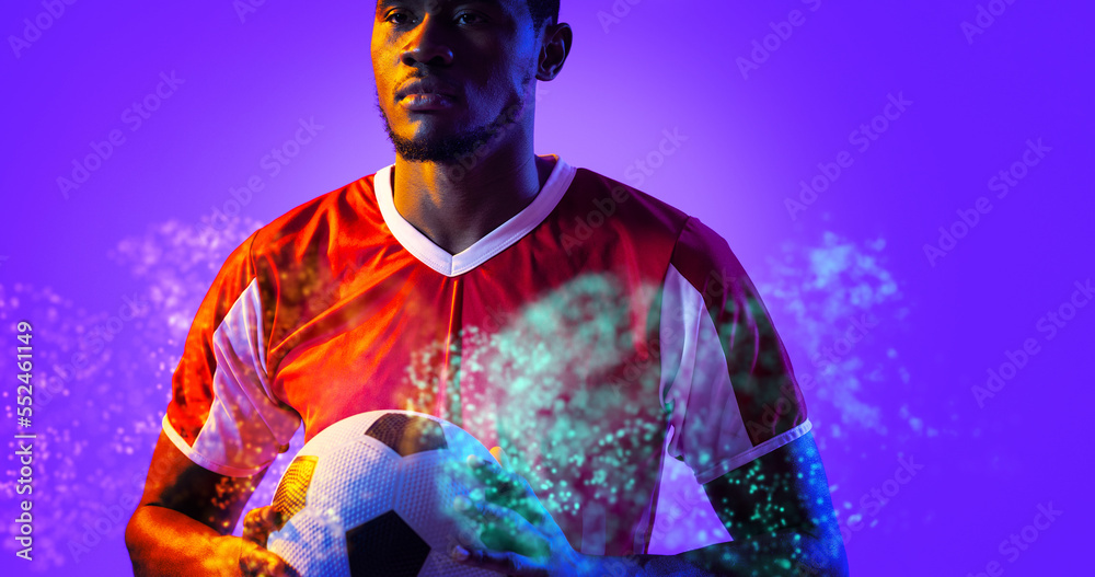 African american male player holding ball amidst illuminated abstract pattern on blue background