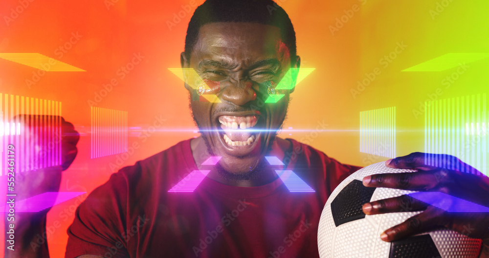 Portrait of african american male fan with ball screaming and shaking fist over colorful lights