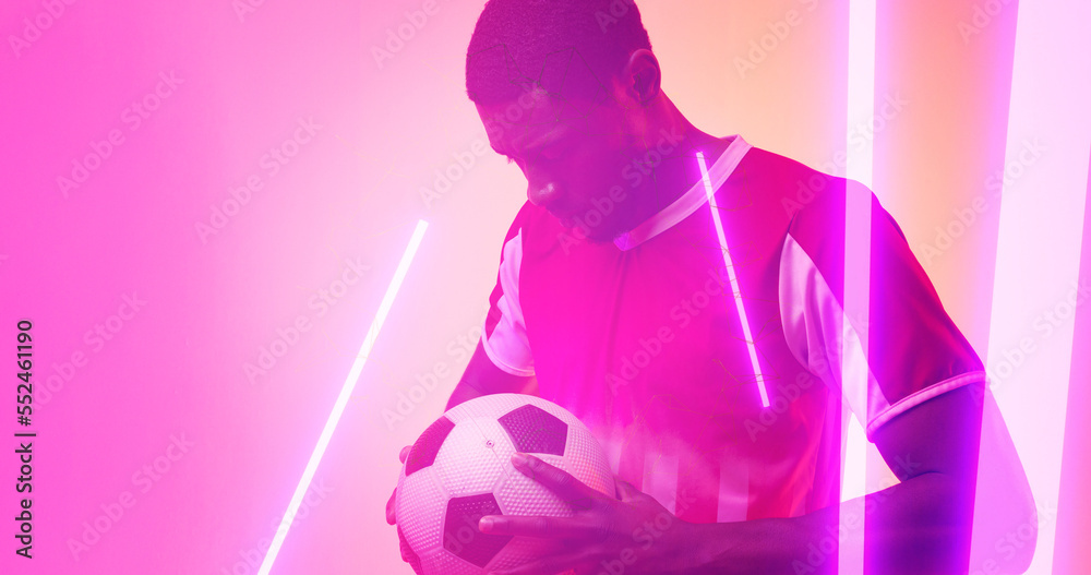 Illuminated lines over serious african american male player holding soccer ball on neon background