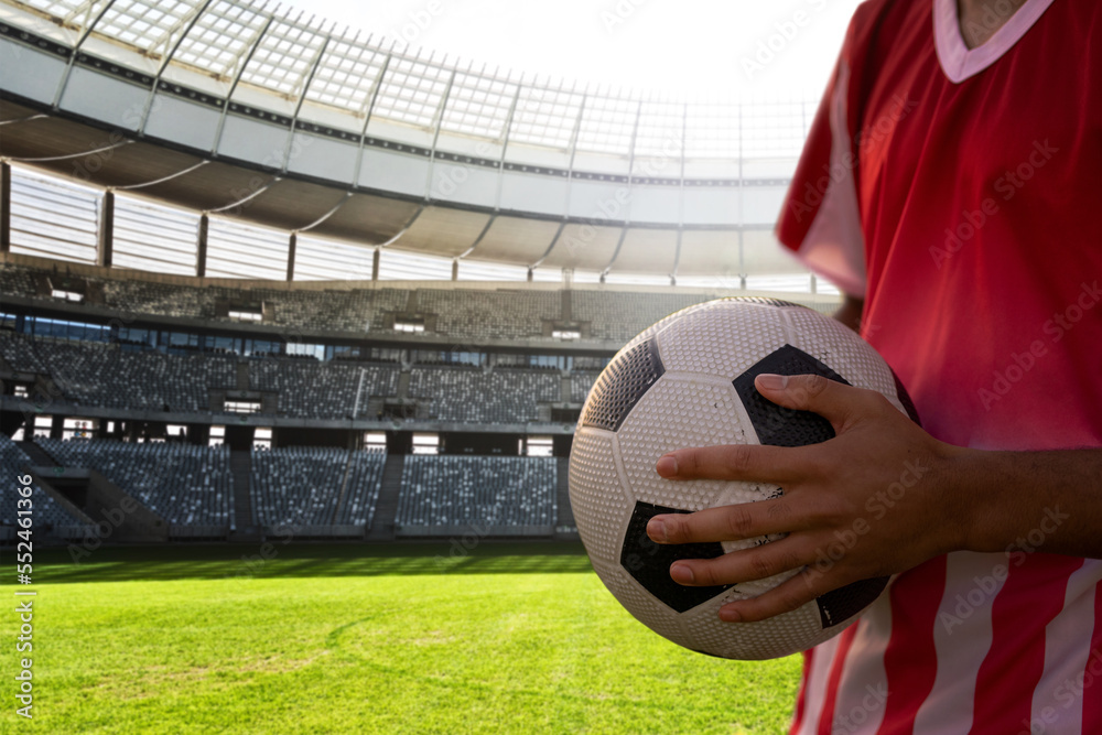 Midsection of player holding soccer ball in stadium on sunny day, copy space