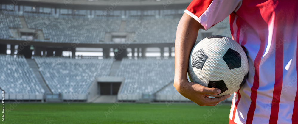 Midsection of player holding soccer ball in stadium, copy space