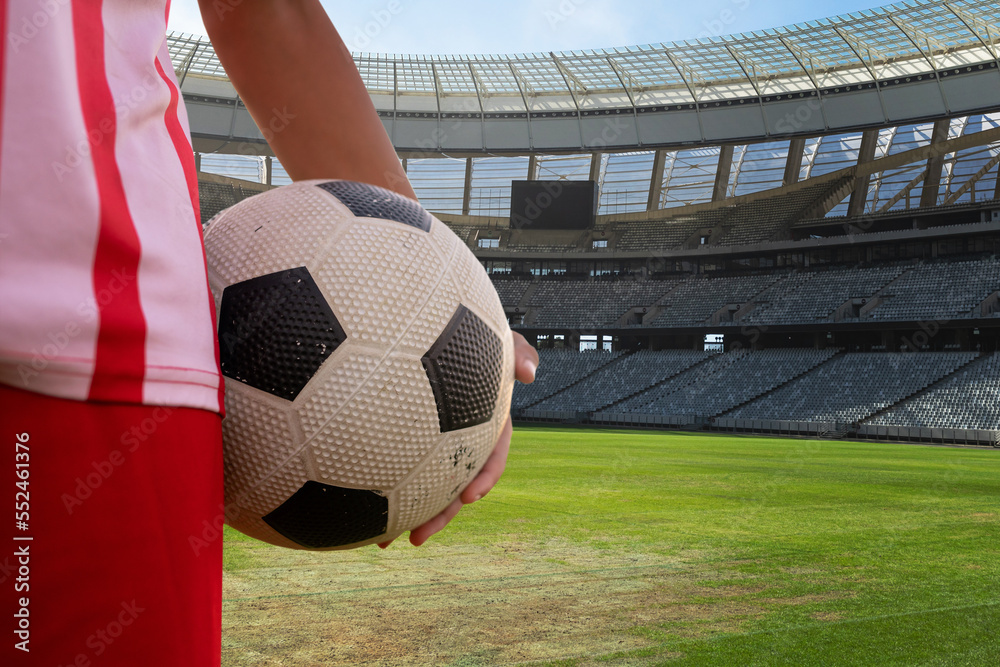 Midsection of player holding soccer ball in stadium during sunny day, copy space