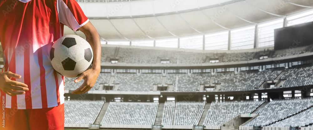 Midsection of player holding soccer ball standing in stadium on sunny day, copy space