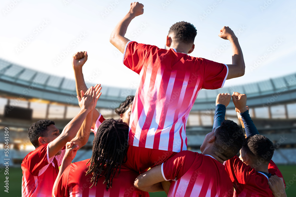 Team of multiracial male players in sports clothing celebrating success in stadium