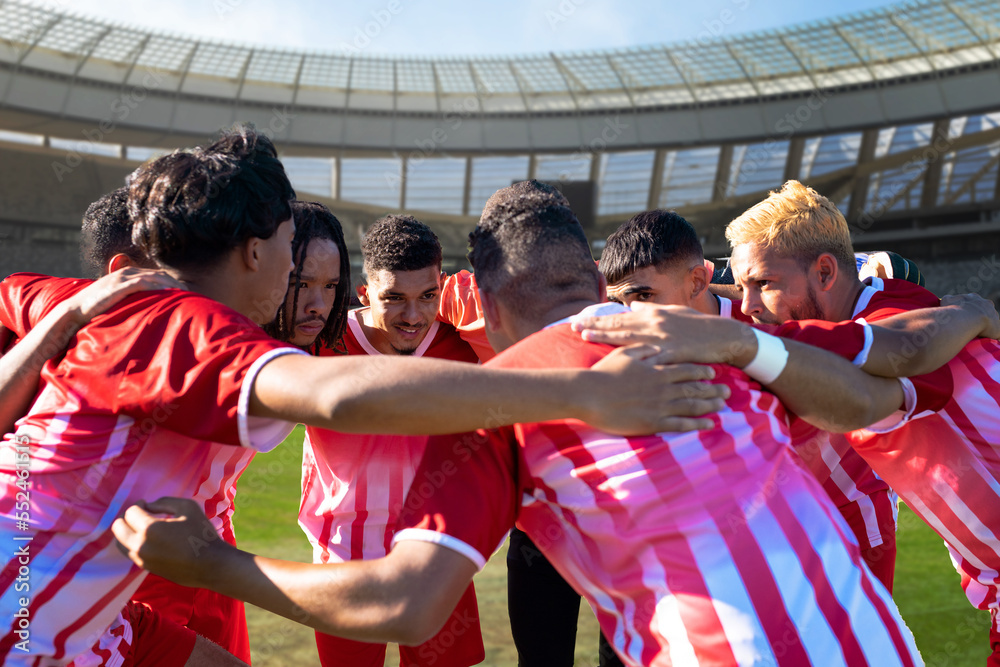 Team of multiracial male players huddling and planning match strategy in stadium