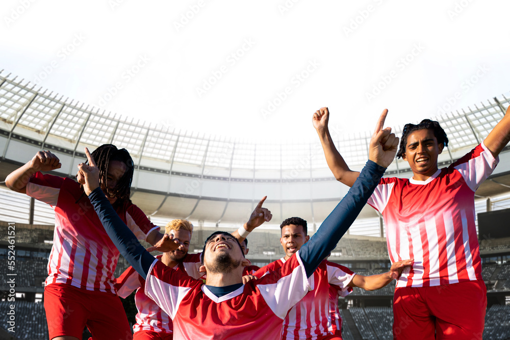 Team of multiracial young soccer players celebrating victory in stadium on sunny day, copy space