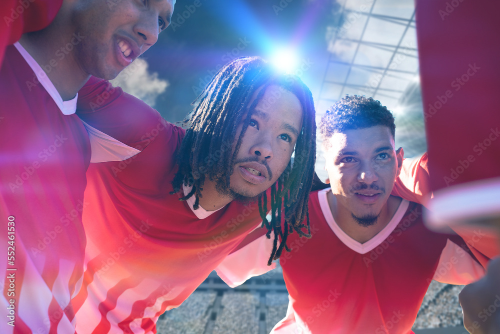 Multiracial young male players huddling and planning match strategy at stadium on sunny day