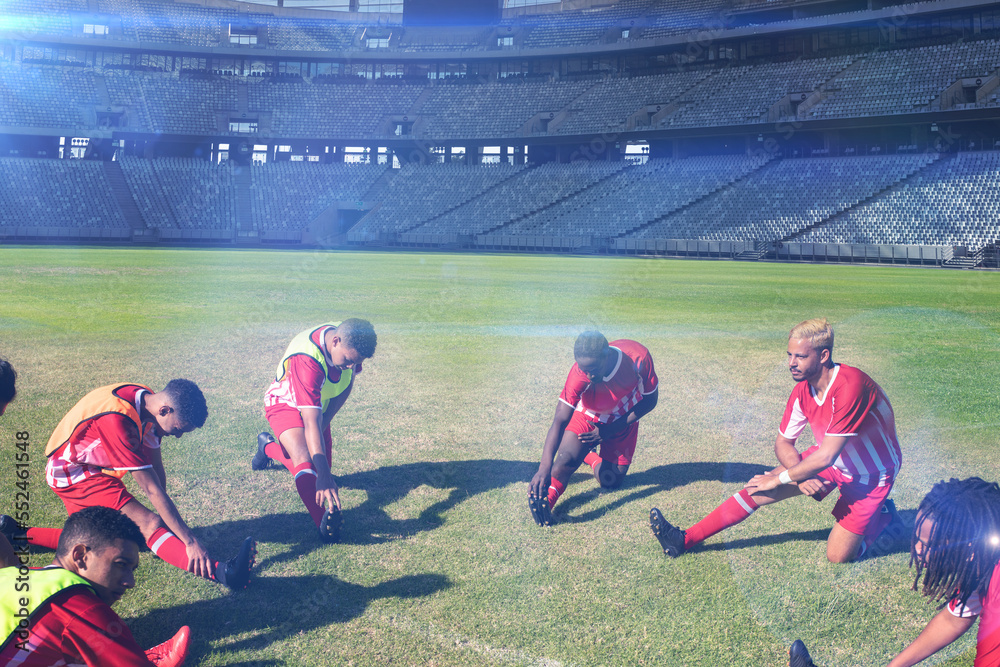 Team of multiracial male players exercising in circle at soccer field on sunny day