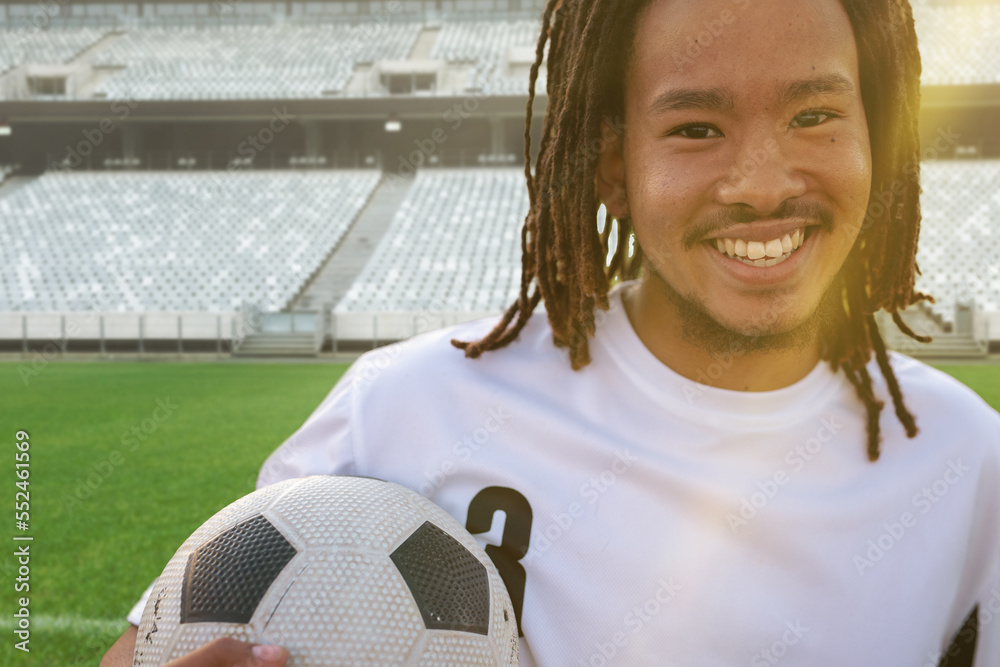 Portrait of smiling african american soccer player with ball at stadium on sunny day