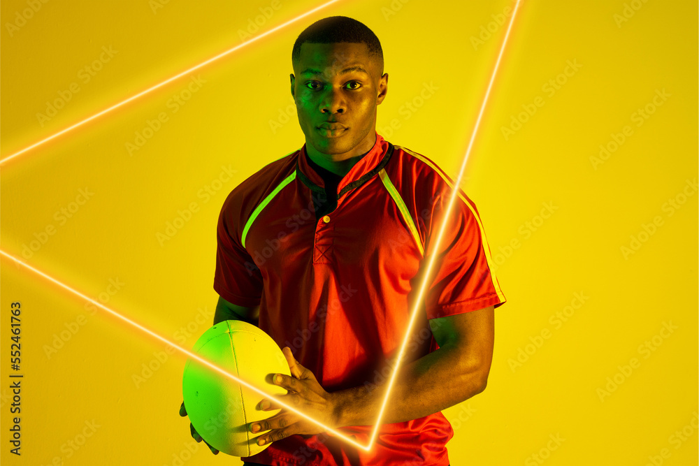 Triangle neon over confident african american young rugby player holding ball on yellow background