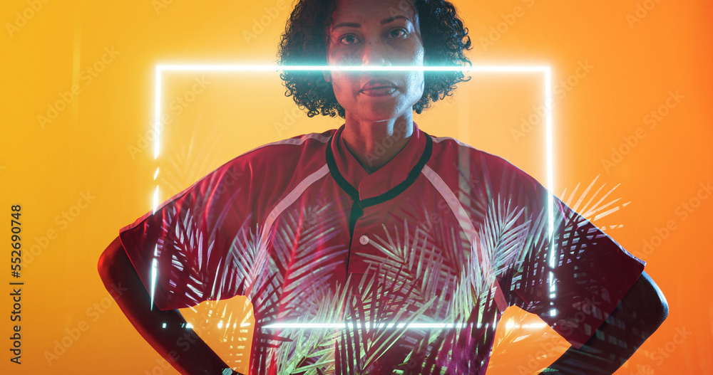 Biracial female rugby player with hands on hip standing over illuminated rectangle and plants