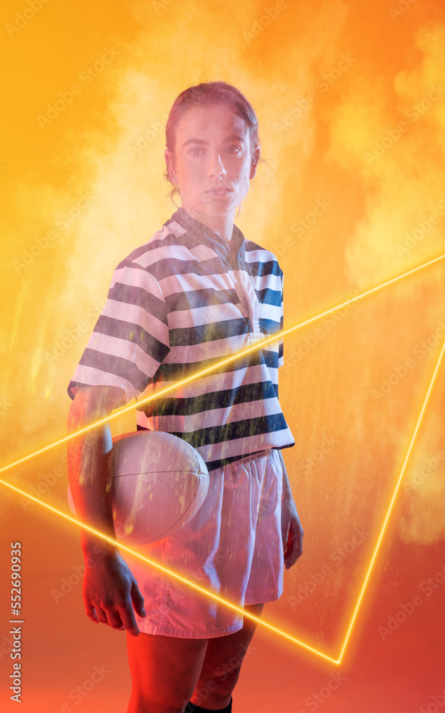 Confident female caucasian player holding ball and standing by illuminated triangle amidst smoke