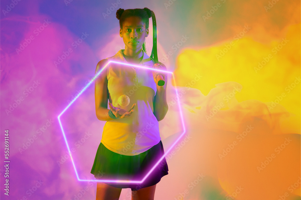 Confident african american female tennis player with racket and ball by illuminated hexagon