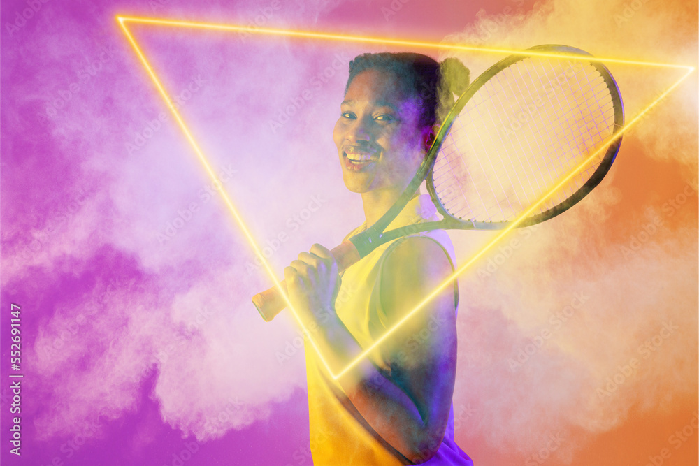 Smiling african american female tennis player with racket amidst smoke by illuminated triangle