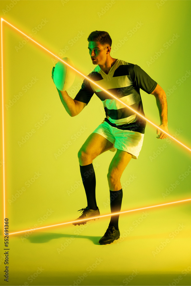 Caucasian male rugby player with ball by illuminated triangle against yellow background