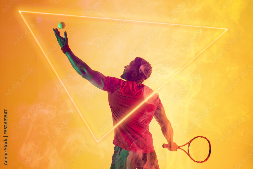 African american male tennis player serving ball with racket by triangle on yellow background