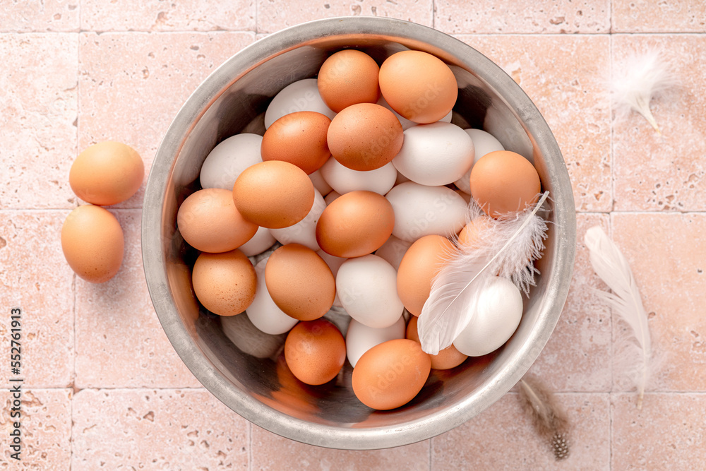 Eggs in metallic bowl on beige background. Top view of raw brown eggs and white eggs with chicken fe