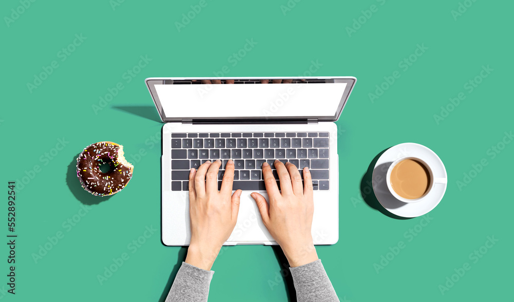 Person using a laptop computer with a donut and a cup of coffee - Flat lay