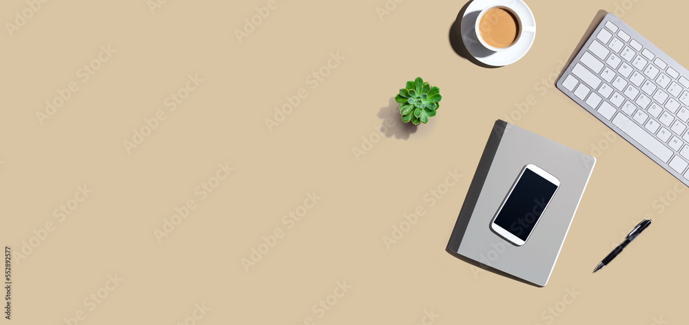 Desk items - keyboard, smart phone, coffee and a pen on a desk from above