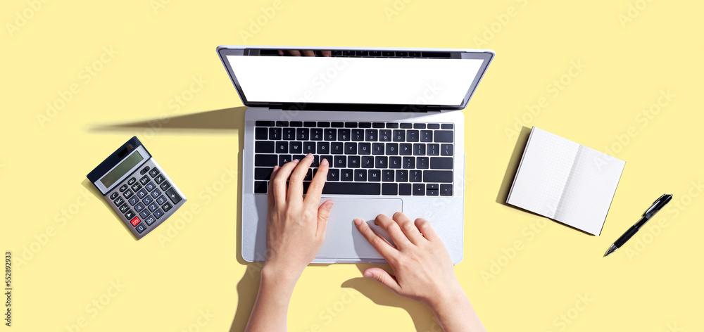 Person using a laptop computer with a notebook and a calculator - flat lay