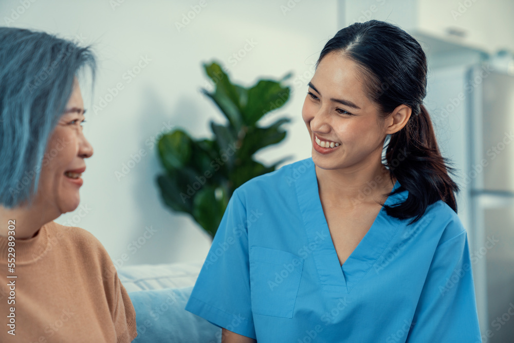 A caregiver rest her hands on the shoulders of a contented senior patient while she sitting on the s