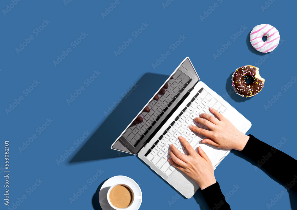 Person using a laptop computer with a donut and a cup of coffee - Flat lay