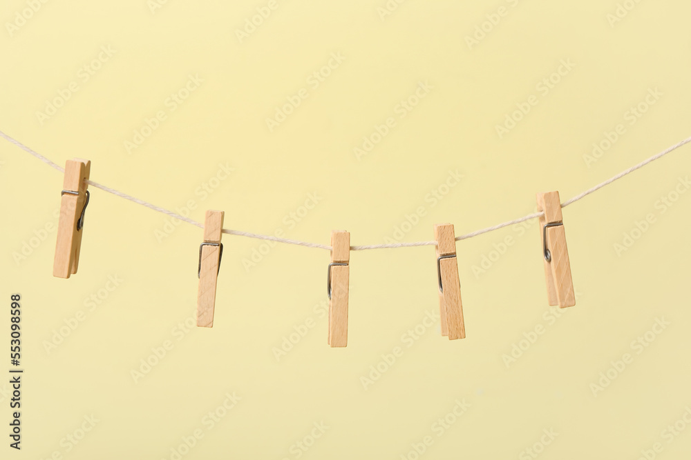 Wooden clothespins hanging on rope against color background