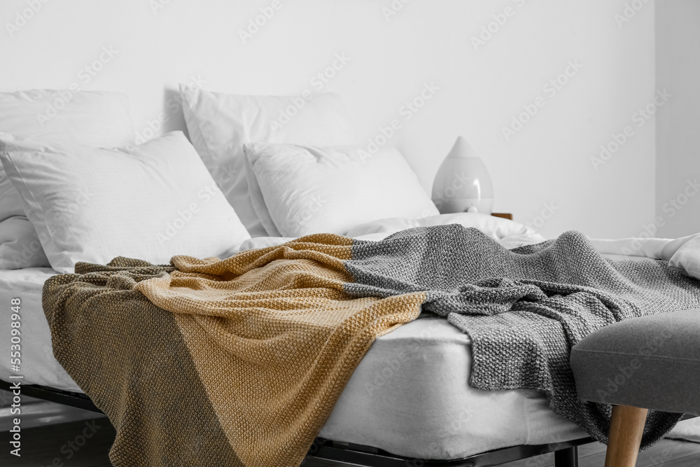 Comfortable bed with white pillows and blanket near light wall