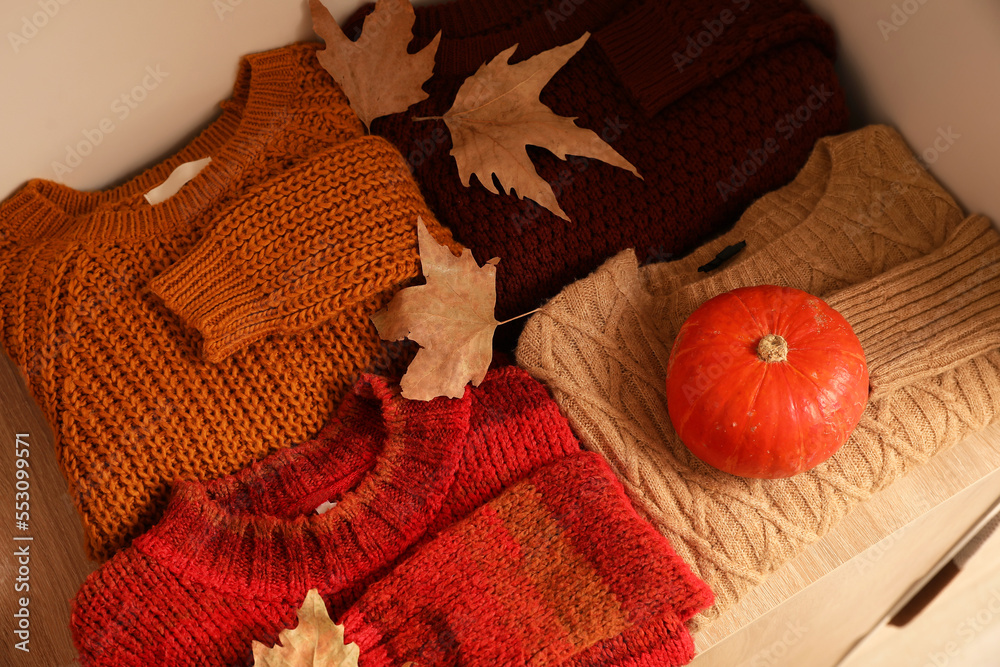 Folded sweaters with autumn leaves and pumpkin on shelf in wardrobe