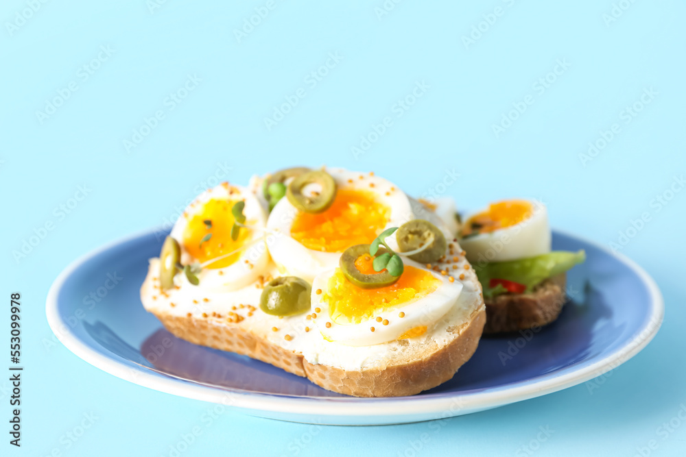 Plate of delicious toasts with boiled egg and olives on color background