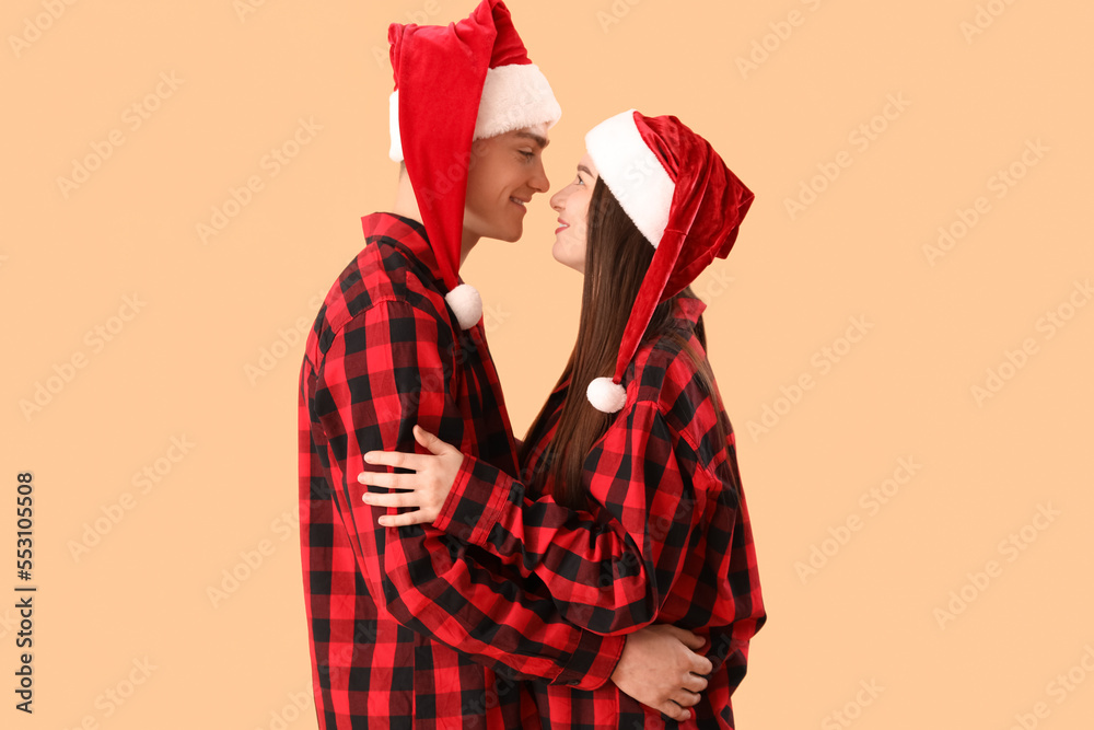 Young couple in Santa hats and pajamas on beige background