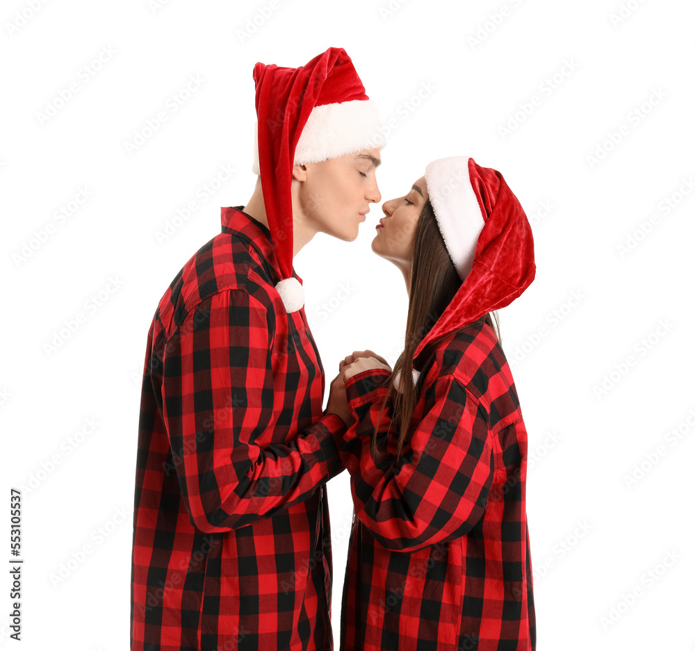 Young couple in Santa hats and pajamas holding hands on white background