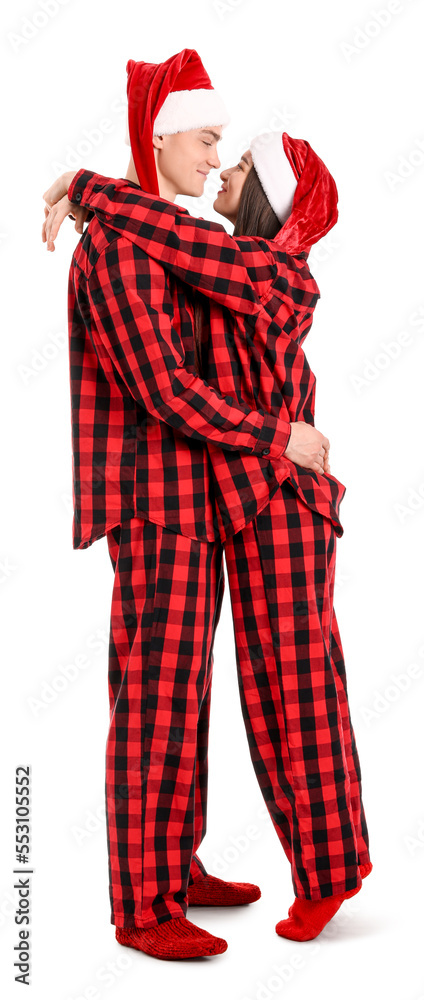 Young couple in Santa hats and pajamas hugging on white background