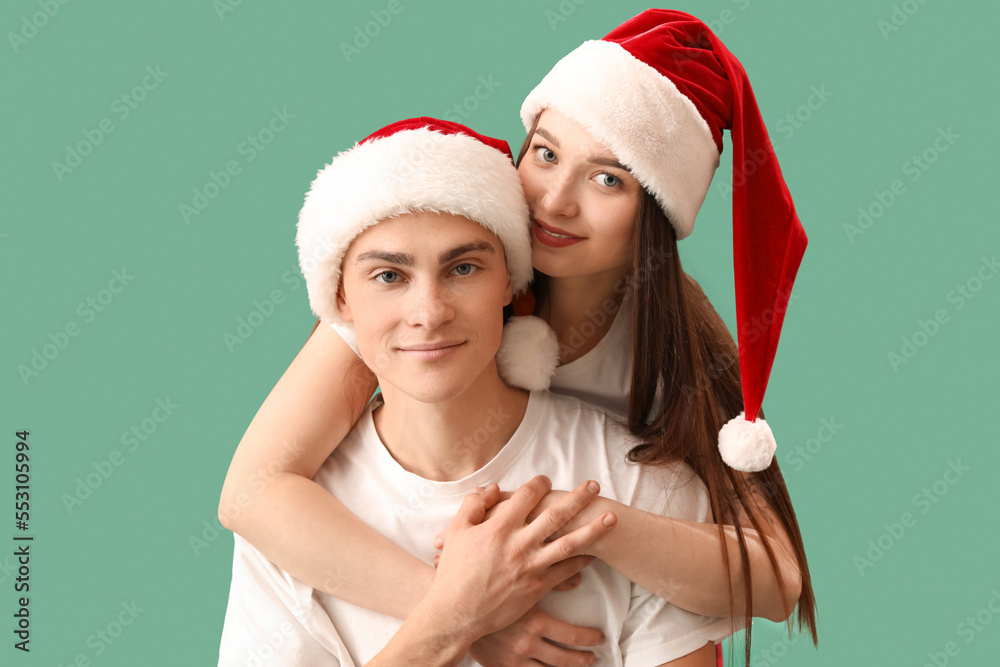 Young couple in Santa hats on green background, closeup