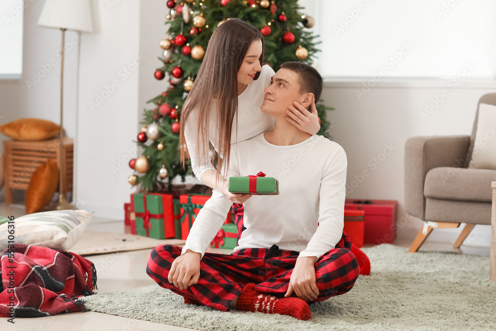 Young woman greeting her boyfriend with Christmas gift at home