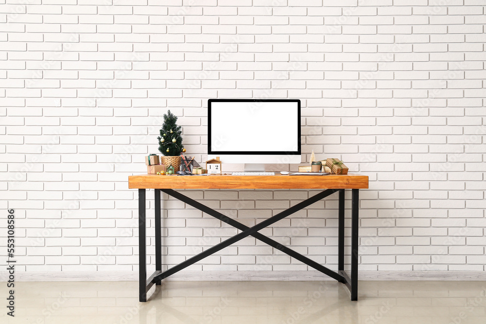 Workplace with computer, Christmas tree and presents near white brick wall