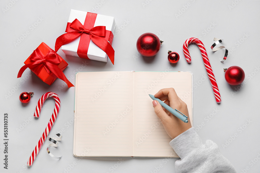 Female hand with blank open notebook, pen, Christmas gifts and decorations on light background