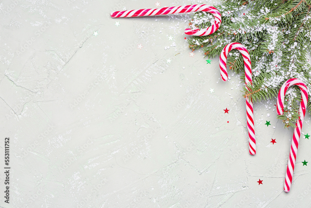 Composition with sweet candy canes, fir branches and snow on light background